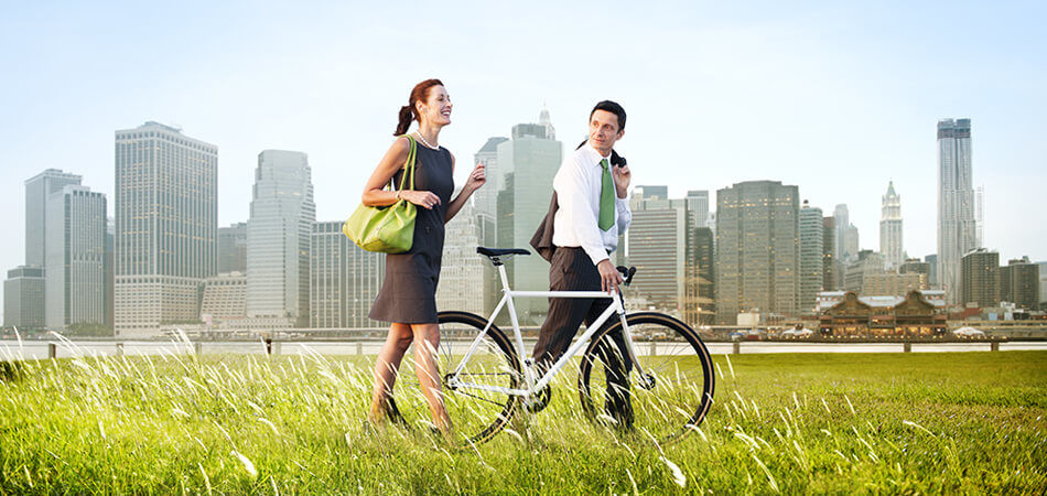 man and woman walking in a field with a bike with a city in the background